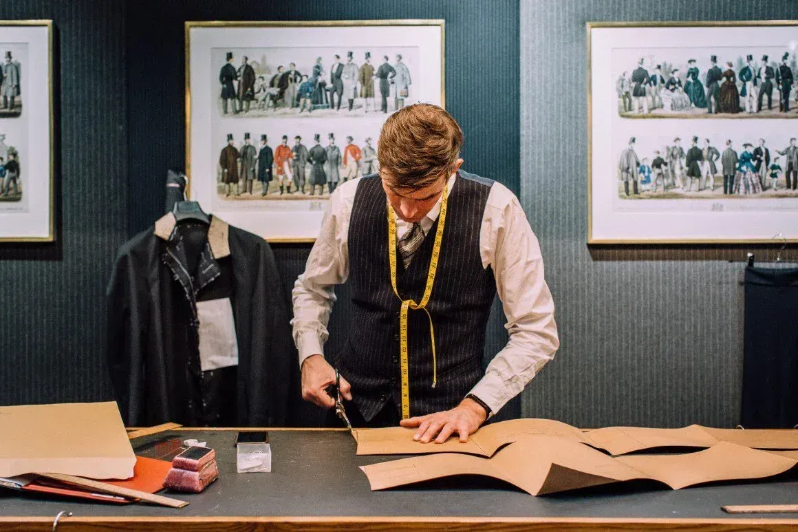 Tailor in a striped waistcoat cutting paper patterns at a workbench