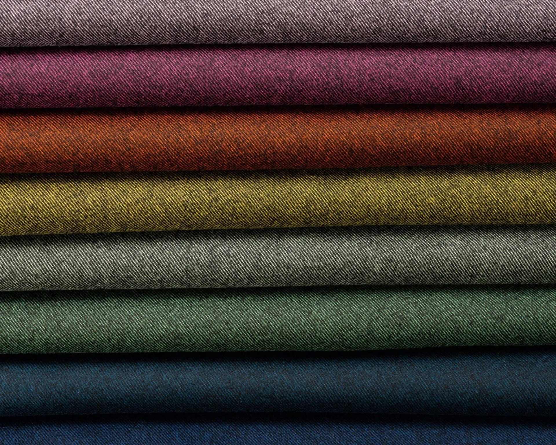 Stack of folded twill fabric bolts in pink, rust, olive, green, and blue