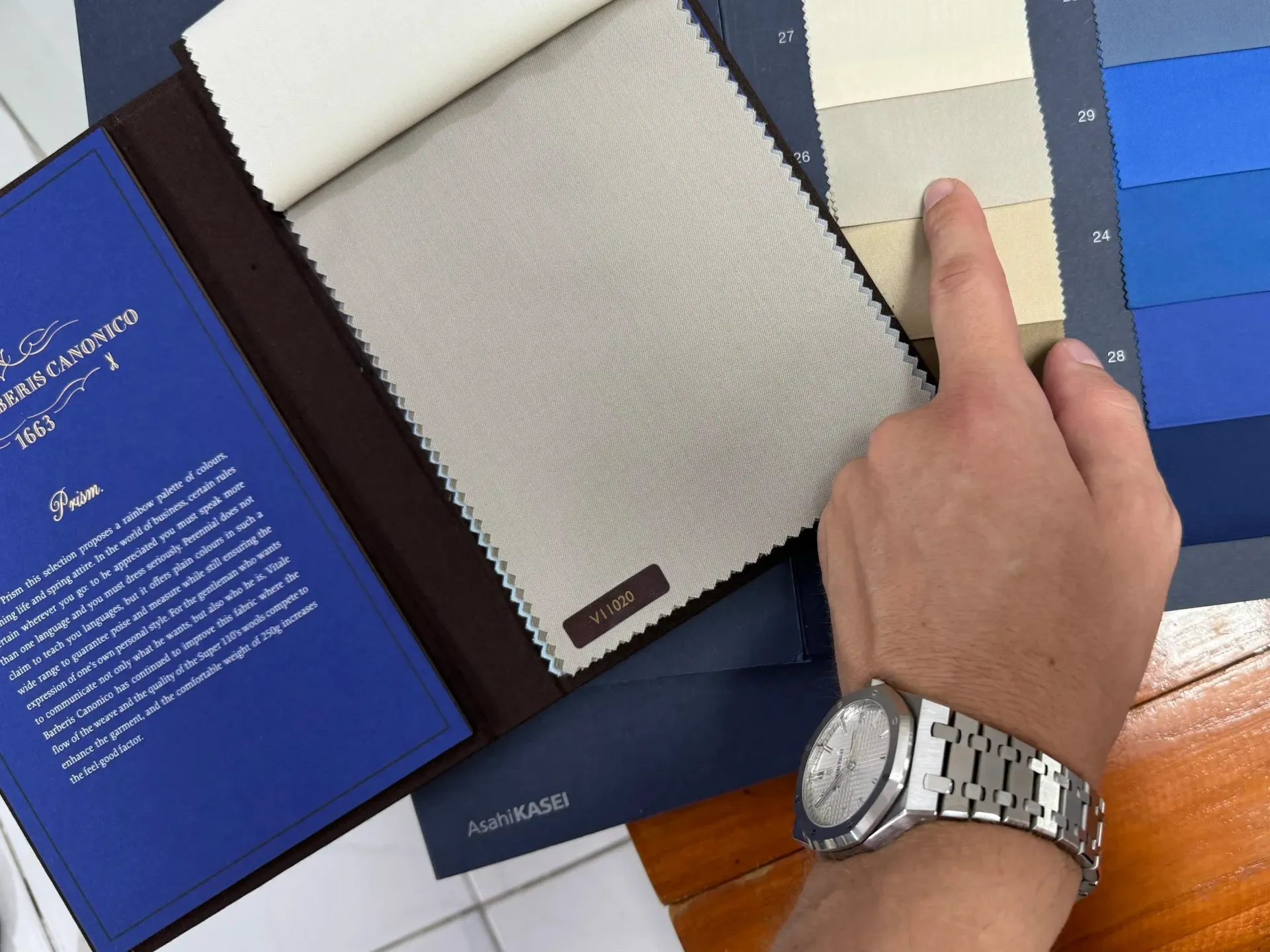 Hand selecting a grey Vitale Barberis Canonico worsted swatch beside graded blue tones
