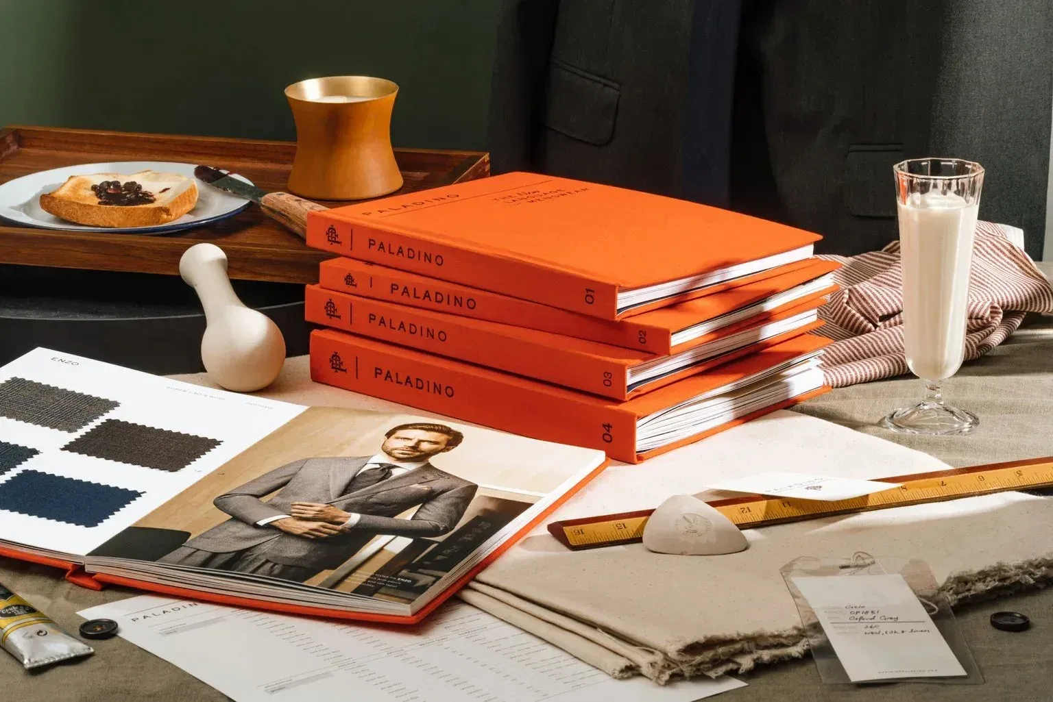 Stacked orange Paladino fabric books with swatches, ruler and tailoring tools on a desk