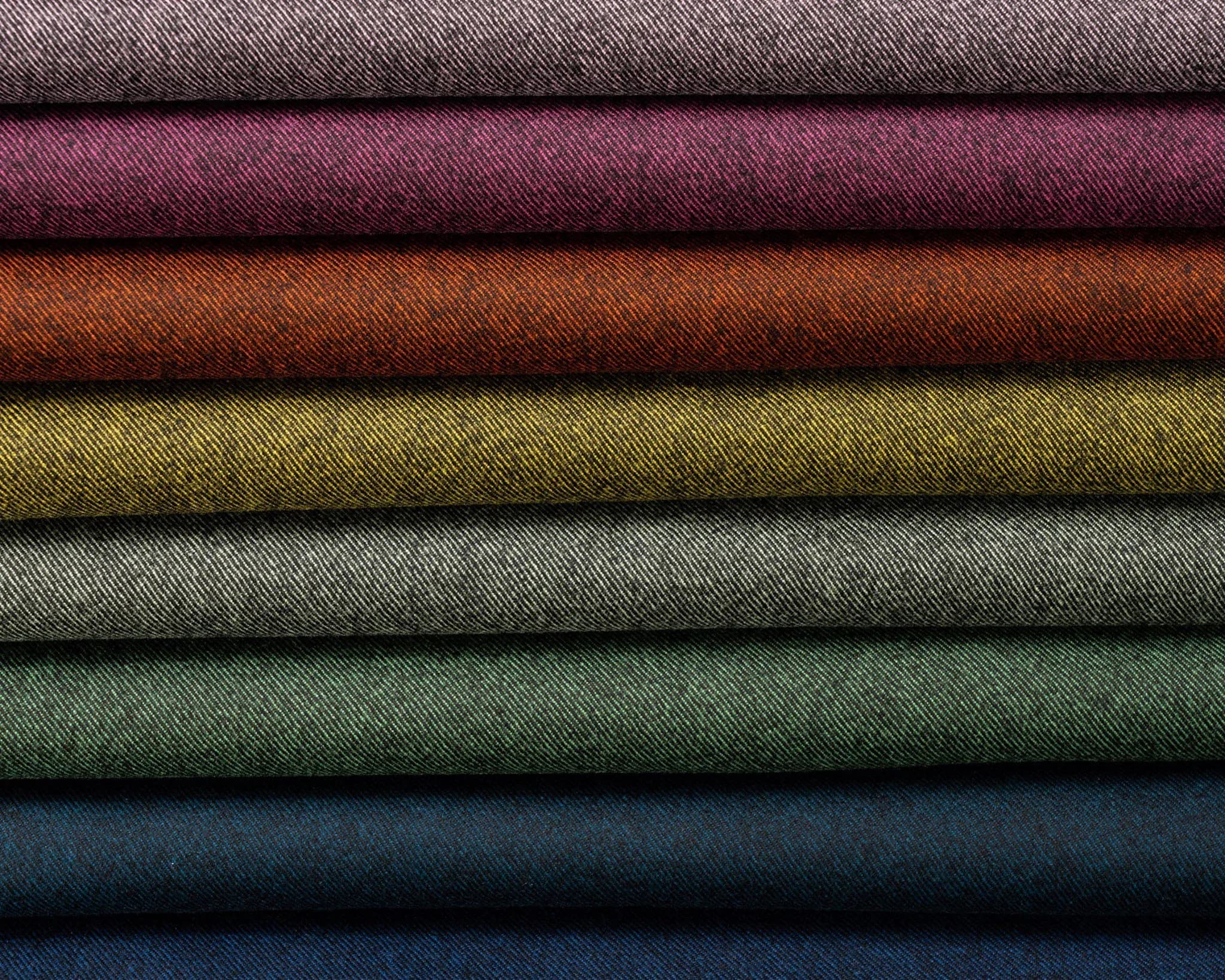Stack of folded twill fabric bolts in pink, rust, olive, green, and blue